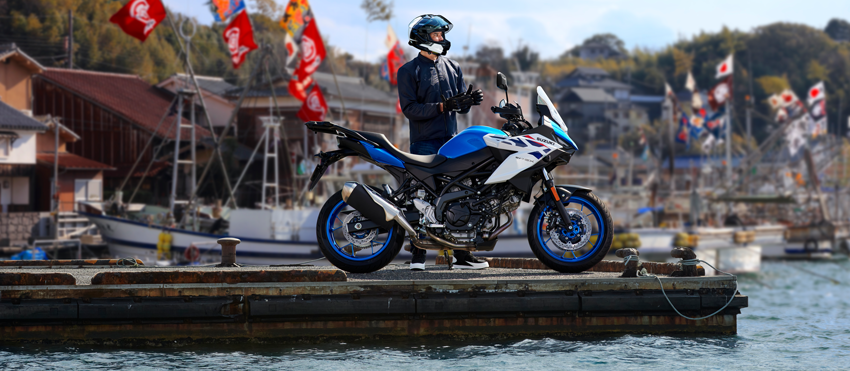 Fahrer steht hinter einer blau-weißen Suzuki SV-7GX auf einem Steg auf dem Wasser.