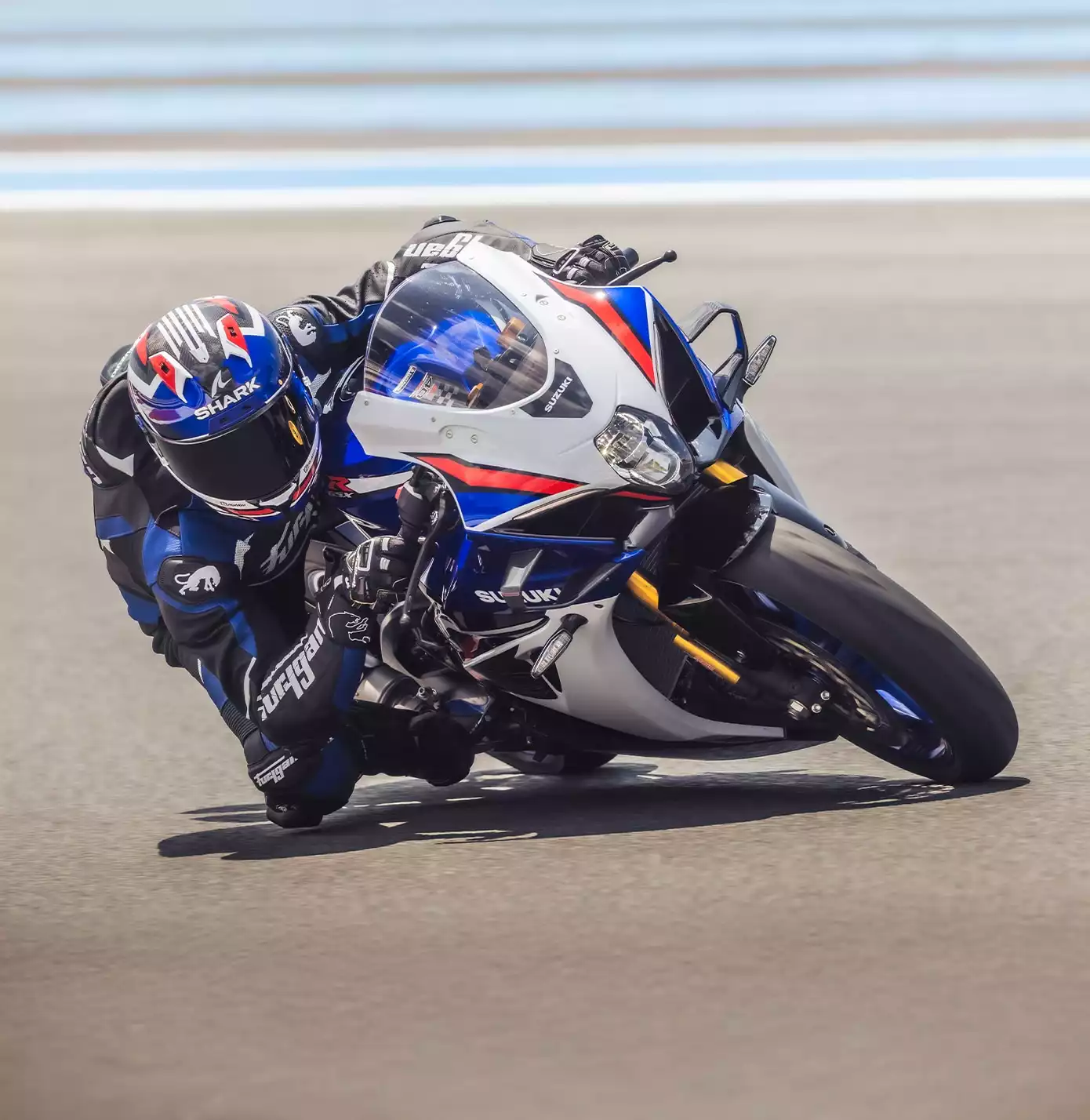 Suzuki GSX-R1000R Sportmotorrad in Weiß-Blau-Rot bei dynamischer Kurvenfahrt auf der Rennstrecke.