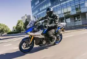 Motorradfahrer auf Suzuki GSX-S1000GT vor modernem Bürogebäude in der Stadt.