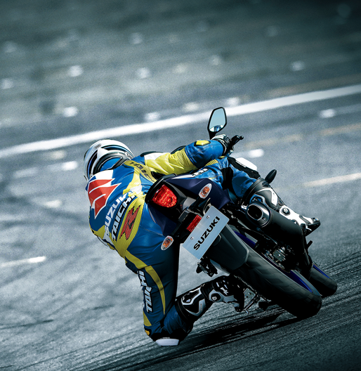 Rückansicht eines Motorradfahrers in blau-gelber Suzuki-Lederkombi, der eine GSX-R125 in Schräglage durch eine Kurve auf der Rennstrecke steuert; Fokus auf das Heck und das Rücklicht.