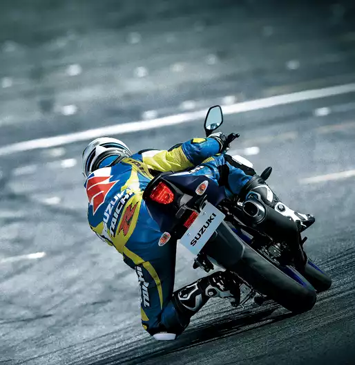 Rückansicht eines Motorradfahrers in blau-gelber Suzuki-Lederkombi, der eine GSX-R125 in Schräglage durch eine Kurve auf der Rennstrecke steuert; Fokus auf das Heck und das Rücklicht.