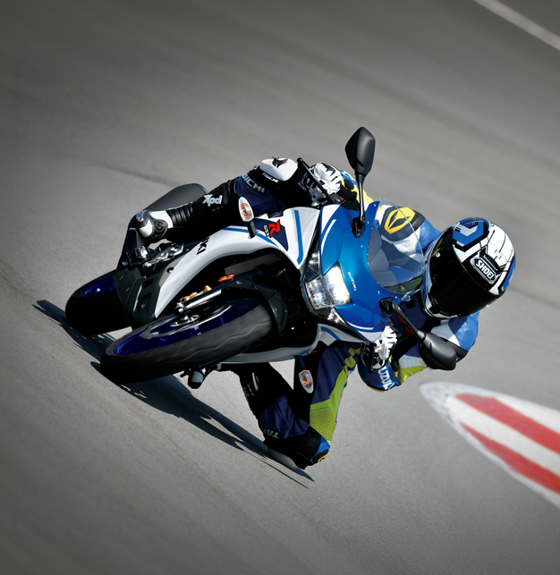 Frontalansicht einer Suzuki GSX-R125 in extremer Schräglage auf einer Rennstrecke, mit einem Fahrer in blau-gelber Lederkombi und Helm.