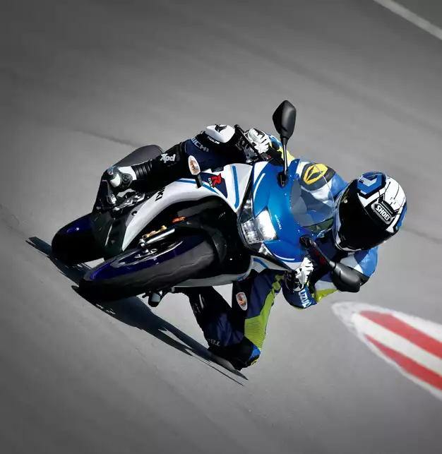 Frontalansicht einer Suzuki GSX-R125 in extremer Schräglage auf einer Rennstrecke, mit einem Fahrer in blau-gelber Lederkombi und Helm.
