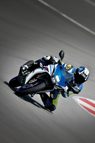 Frontalansicht einer Suzuki GSX-R125 in extremer Schräglage auf einer Rennstrecke, mit einem Fahrer in blau-gelber Lederkombi und Helm.