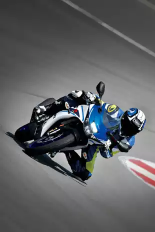 Frontalansicht einer Suzuki GSX-R125 in extremer Schräglage auf einer Rennstrecke, mit einem Fahrer in blau-gelber Lederkombi und Helm.