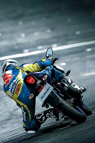 Rückansicht eines Motorradfahrers in blau-gelber Suzuki-Lederkombi, der eine GSX-R125 in Schräglage durch eine Kurve auf der Rennstrecke steuert; Fokus auf das Heck und das Rücklicht.