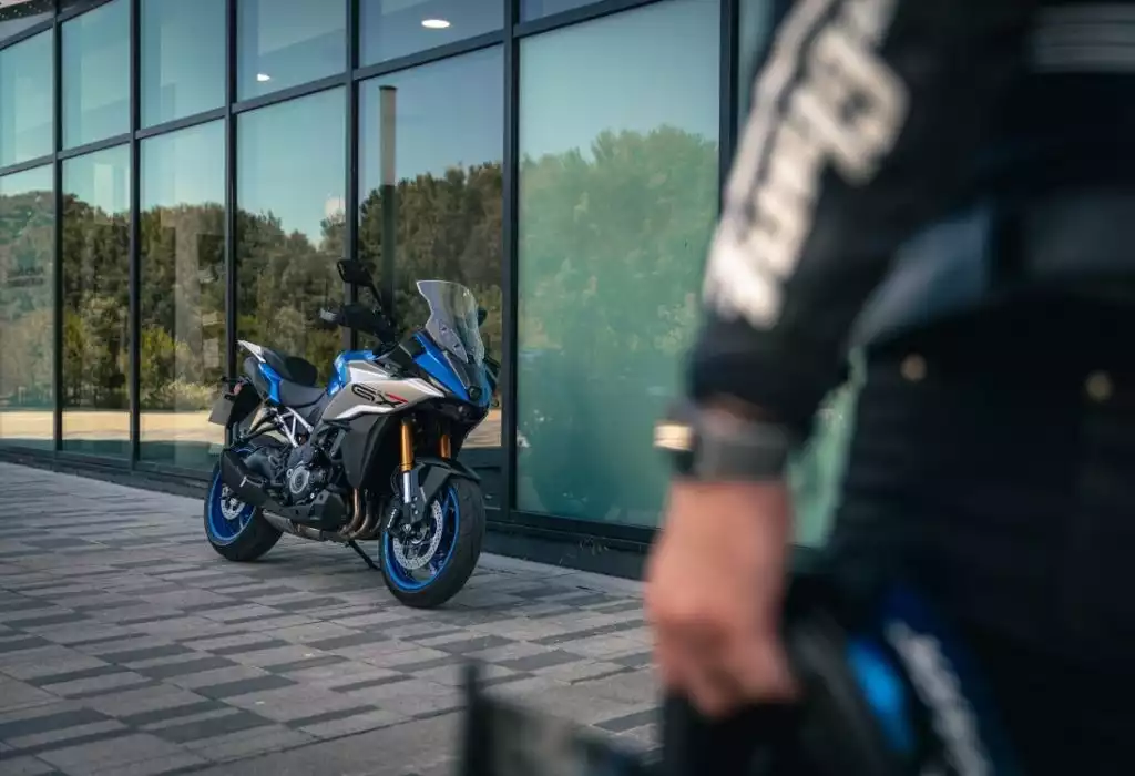 Blaue Suzuki GSX-S1000GX mit Fahrer vor modernem Gebäude.