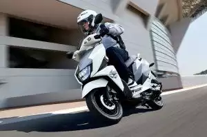 Fahrer auf Suzuki Avenis 125 Roller vor moderner Architektur