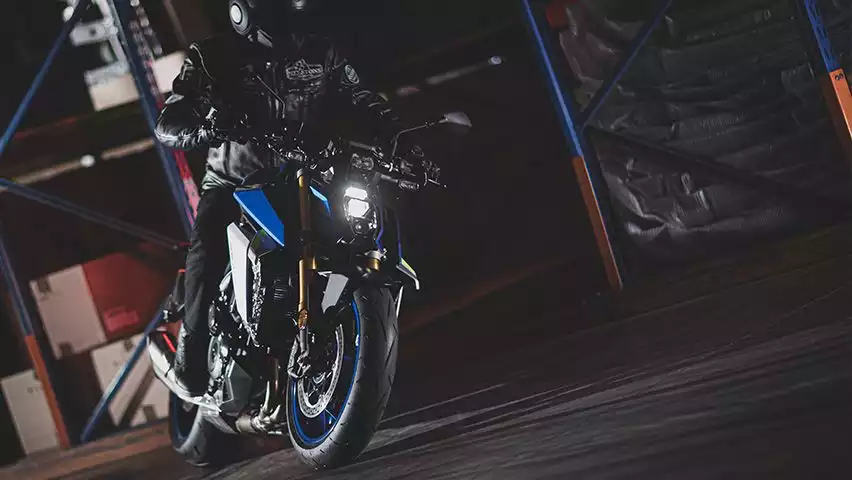 Fahrer in dunkler Lagerhalle auf blauer GSX-S1000, die hellen LED-Scheinwerfer betonen ihr sportliches Design.