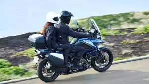 Paar fährt auf blauer Suzuki V-Strom 1050 mit Top- und Seitenkoffern auf malerischer Küstenstraße.