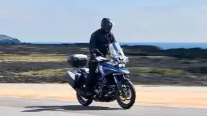 Fahrer auf blauer Suzuki V-Strom 1050 mit Topcase und Seitenkoffern auf malerischer Küstenstraße.