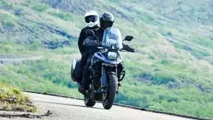 Paar fährt auf blauer Suzuki V-Strom 1050 mit Seitenkoffern auf einer kurvigen Bergstraße.