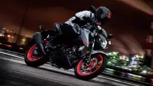 Suzuki Naked Bike in Schräglage bei Nacht, rote Felgen, dynamische Fahrt durch die Stadt.