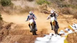 Zwei Motocross-Fahrer auf gelben Suzuki RM-Z250 Bikes in voller Fahrt auf staubiger Offroad-Strecke.