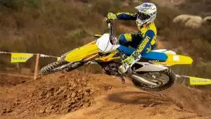 Motocross-Fahrer auf gelber Suzuki RM-Z250 springt dynamisch über einen Erdhügel auf der Rennstrecke.