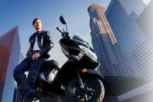 Mann sitzt auf schwarzem Suzuki Burgman Street 125EX Roller in urbaner Skyline, repräsentiert stilvolle Stadtmobilität.